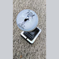 Lady Luck resin shifter ball installed on a vehicle shifter — angled overhead view showing the black-on-white vintage Lady Luck pinup artwork and banner on a gloss white resin ball. Chrome shift boot plate below on concrete surface. 
