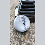 Lady Luck handmade resin shifter ball resting on concrete with shift boot plate in background — gloss white resin body showing the black vintage Lady Luck pinup artwork and banner. Uninstalled display view.