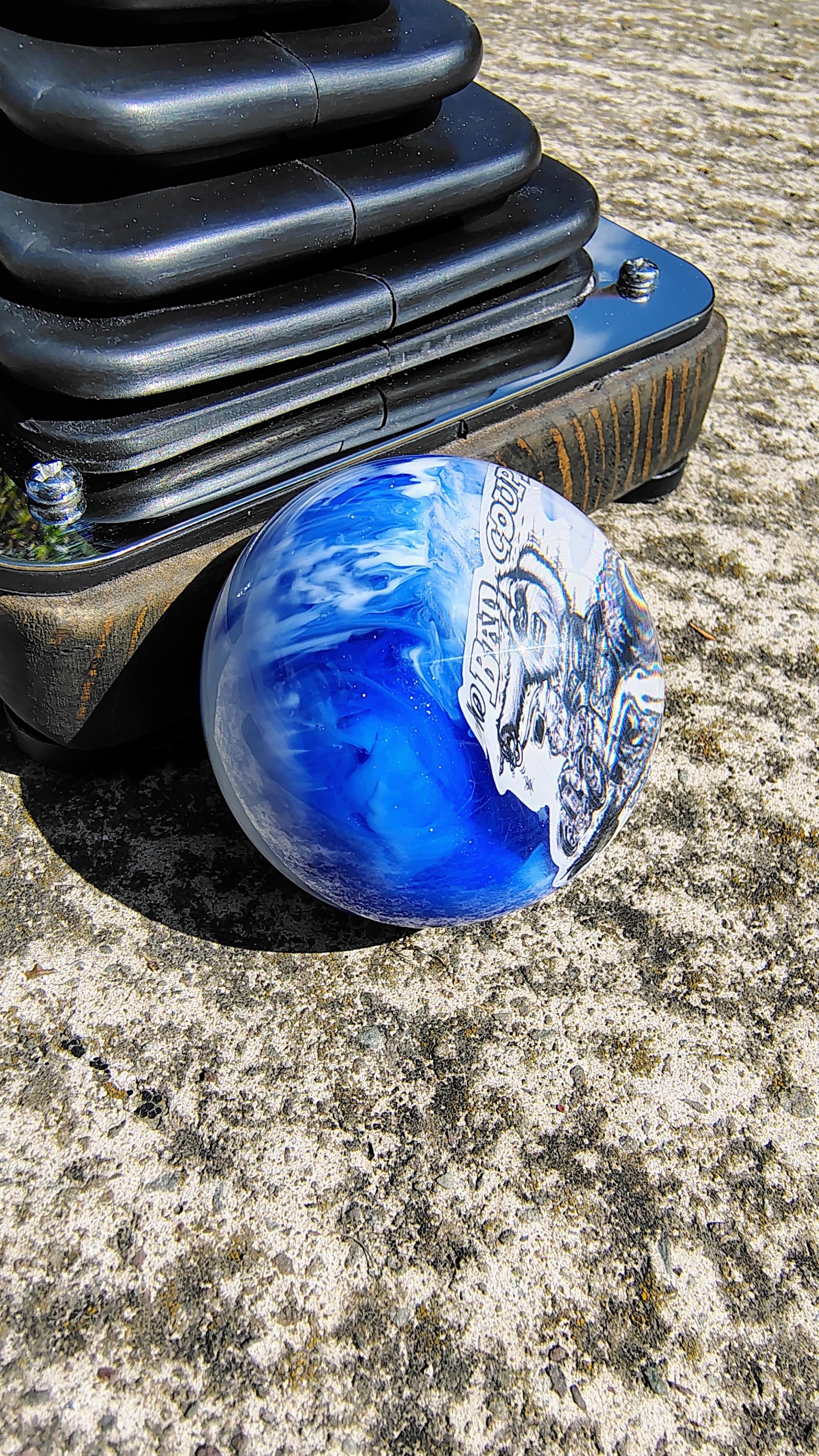 Side view of The Bad Coupe Resin Shifter Ball showing the swirled blue and white marbled resin finish and the gloss clear dome over the artwork