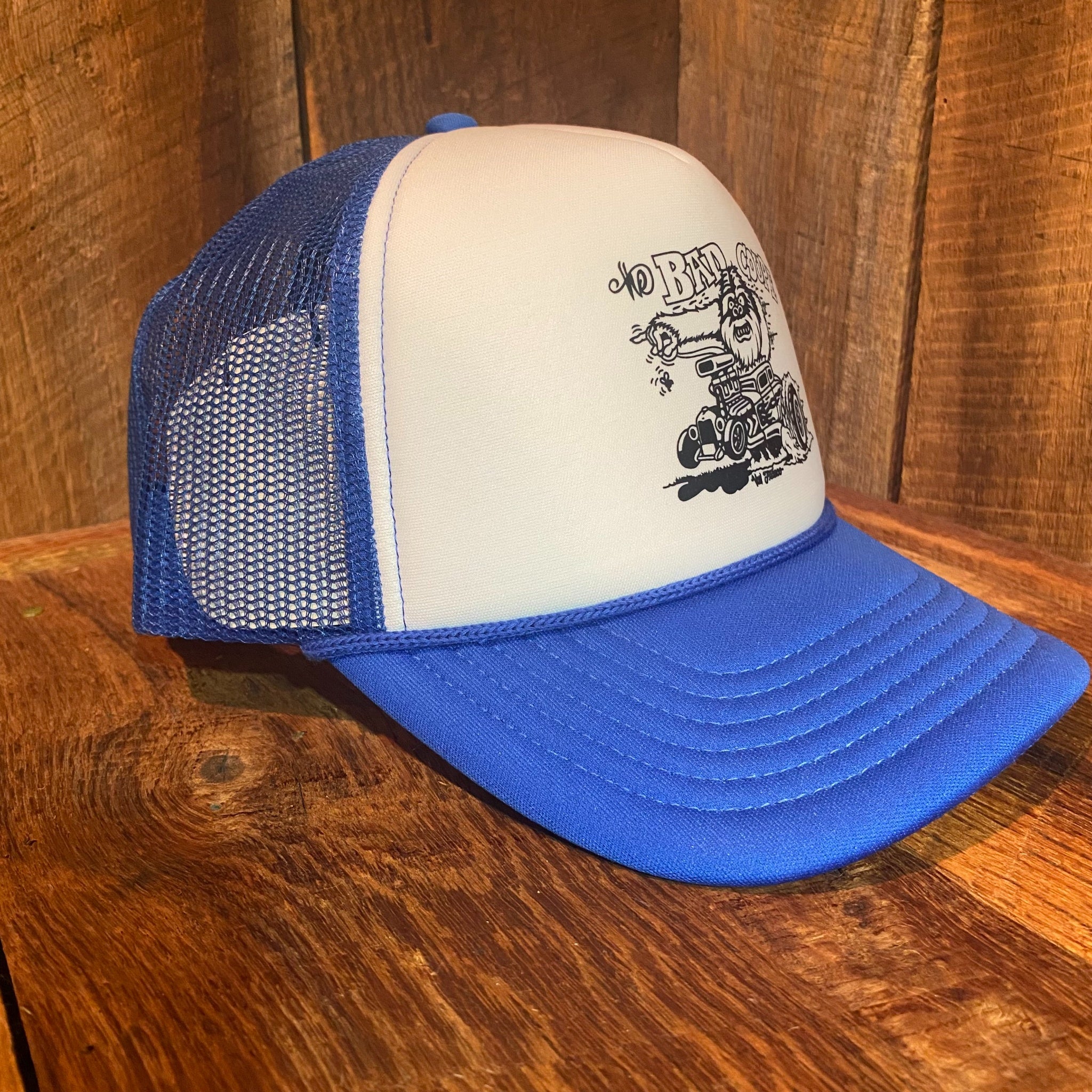 Left side view of The Bad Coupe Yeti Foam Trucker Hat in blue and white, showing the foam front profile and breathable mesh back