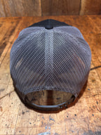 Top-down view of the Pudding Creek charcoal trucker hat showing the grey polyester mesh back panels and circular snapback closure ring, photographed on a rustic wooden surface.