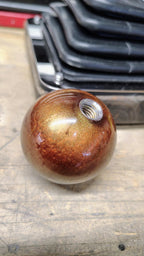 Underside of the Pudding Creek Rod Shop resin shifter ball showing the stainless steel threaded insert used for mounting on a shift lever. The ball features a swirled metallic bronze and gold resin finish with gold flake sparkle throughout.