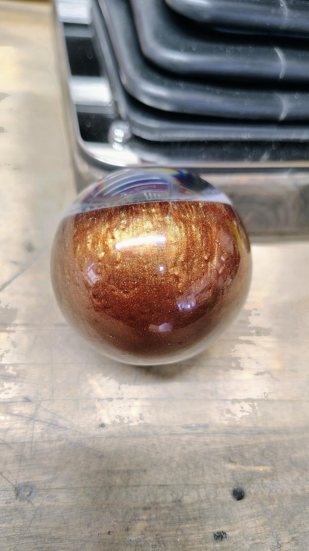 Close-up front view of the Pudding Creek Rod Shop resin shifter ball showing the handcrafted metallic bronze and gold swirl resin finish with sparkling flake and a deep gloss clear coat.